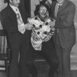 Flash Harry (Derek Dearne) and Alf Tubbe (Keith Beattie) carry jockey Fred Fipps (Bob Johnson) back into the room.