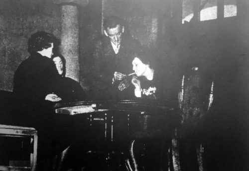 Dr. Jeefries (Ted Younghusband) lights a cigarette for Sarat during a hand of bridge